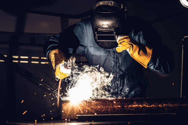 Metal welder working with arc welding machine to weld steel at factory while wearing safety equipment. Metalwork manufacturing and construction maintenance service by manual skill labor concept.