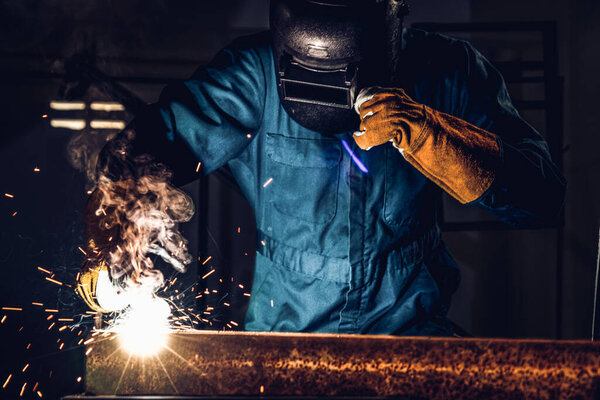 Metal welder working with arc welding machine to weld steel at factory while wearing safety equipment. Metalwork manufacturing and construction maintenance service by manual skill labor concept.