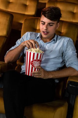 Genç bir adam sinemada film izlerken patlamış mısırla eğleniyor.